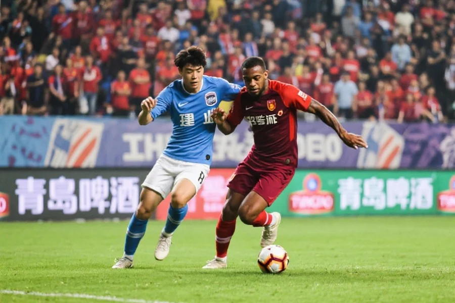 中超联赛中，一位本土球员与外援在比赛中合作进攻，背景为满座球迷，动作激烈